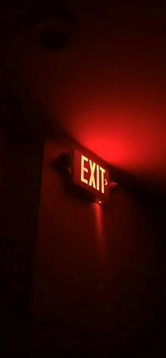 an exit sign is lit up in the dark with red light coming from underneath it