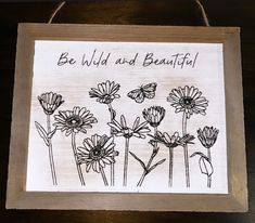 a wooden sign with flowers and the words be wild and beautiful written in black ink