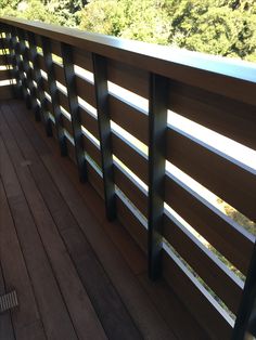 a wooden deck with metal railings and trees in the background