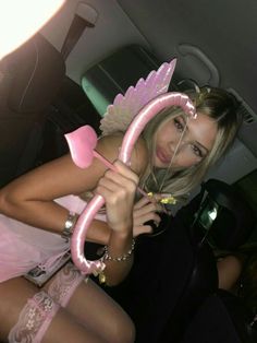 a beautiful young lady holding onto a pink object in her hand while sitting on the back seat of a car