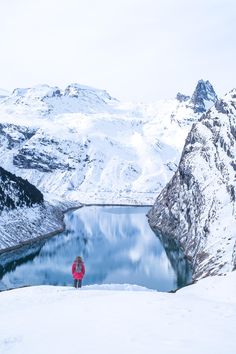 a person standing on top of a snow covered hill next to a lake and mountains