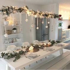 a white table with candles and greenery on it in the middle of a kitchen