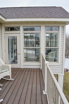 a white rocking chair sitting on top of a wooden deck next to a door and windows