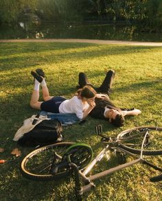 two people laying on the grass with their bikes