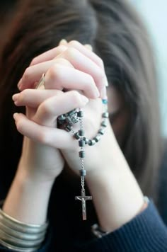 a woman holding her hands to her face while wearing a rosary