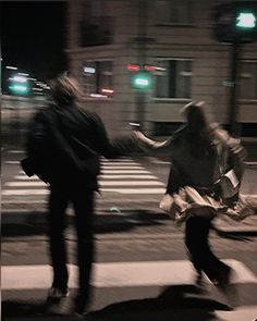 two people crossing the street at night with their hands in each other's pockets