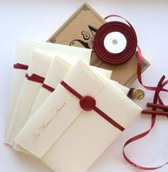 four cards with red ribbon and button on them, sitting next to a white candle