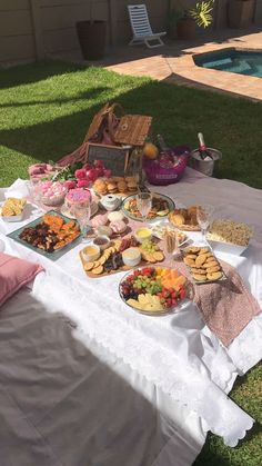 a table full of food sitting on top of a lush green field next to a swimming pool