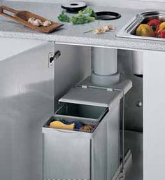 a kitchen sink with two trash cans in the middle and some vegetables on the counter