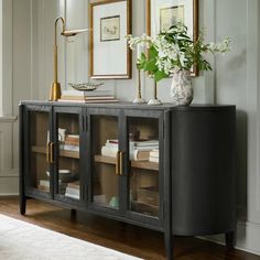 a black sideboard with glass doors and flowers in vases on the top shelf