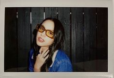 a woman wearing glasses standing in front of a wooden wall with her hand on her chin