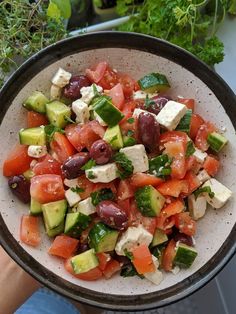 a bowl filled with cucumber, tomatoes and olives next to some herbs