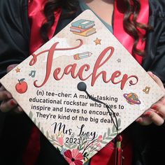 a woman wearing a graduation cap and gown holding a sign with the words teacher on it