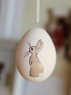 an egg with a drawing of a rabbit on it hangs from a string in front of a white wall