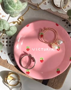 a pink plate with two rings on it next to other jewelry and ring holder items