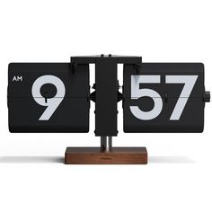 a black clock with white numbers is on a wooden base and stands in front of a white background