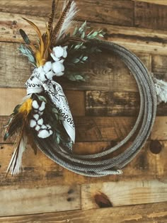 a wreath made out of rope and feathers on top of a wooden wall with white flowers