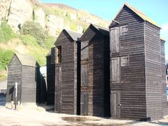 three wooden buildings sitting next to each other in front of a mountain side with trees