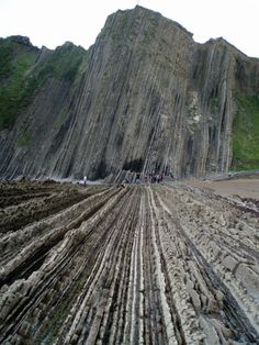 people are standing on the beach next to large rocks and cliffs that look like they have been cut down