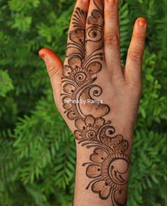 a hand with henna tattoos on it and green plants in the backgroud