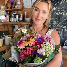 a woman holding a bouquet of flowers in front of a chalkboard