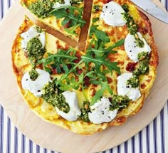 a pizza with cheese, broccoli and spinach on it next to a knife