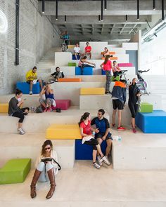 many people are sitting and standing on the stairs in an open space with colorful steps