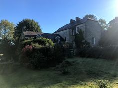 an old stone house surrounded by trees and bushes on a sunny day with the sun shining