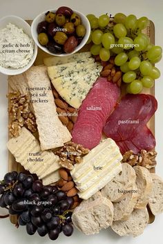 an assortment of cheeses, meats and grapes on a board