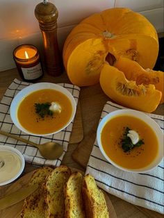 two bowls of soup on a table with pumpkins and other items around it, including bread