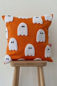 an orange pillow with white ghost faces on it, sitting on a wooden chair in front of a wall