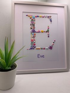 the letter e is made up of small buttons and beads, next to a potted plant