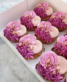 cupcakes with pink frosting in a box on a marble counter top,