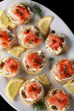 small appetizers are arranged on a plate with lemon wedges and dill