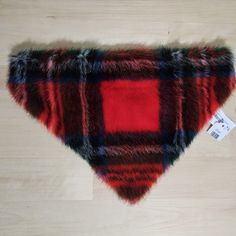 a red and black plaid dog bandana on a wooden floor with a tag attached to it