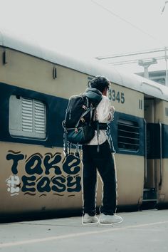 a man standing in front of a train with a back pack on his shoulder and looking down at the ground