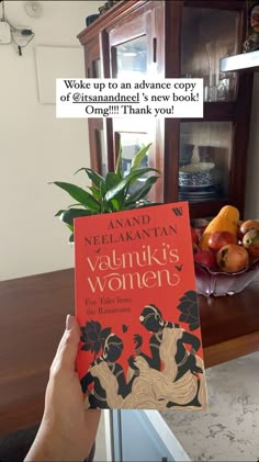 a person holding up a book in front of a table full of fruit and vegetables