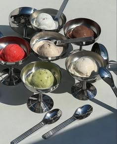 an array of spoons and bowls with ice cream in them on a white surface