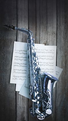 a saxophone sitting on top of sheet music next to a wooden wall with sheet music