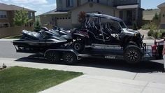 a couple of people standing next to a black and silver truck with jet skis on it