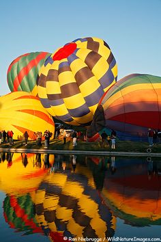 many colorful hot air balloons are reflected in the water as people stand near them and watch