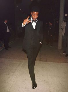 a man in a tuxedo is walking on the sidewalk and pointing at something