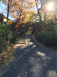 the sun shines brightly through the trees on this road that is lined with leaves