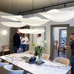 three people standing around a table in a room with chairs and chandeliers hanging from the ceiling