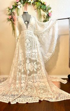 a white wedding dress on display in front of a wall with flowers and greenery