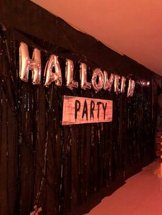 balloons and streamers decorate the entrance to a halloween party with black curtains, silver foil fringes and a sign that says hallow party