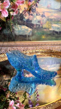 a blue glass shoe sitting on top of a gold plate next to flowers and paintings