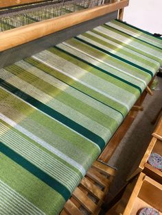 an old weaving machine with green and white striped fabric on the loom, next to some wooden drawers