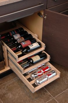 an open drawer with several bottles of wine in it on the floor next to a counter