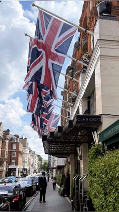 an union jack flag hanging from the side of a building next to a sidewalk with cars parked on it